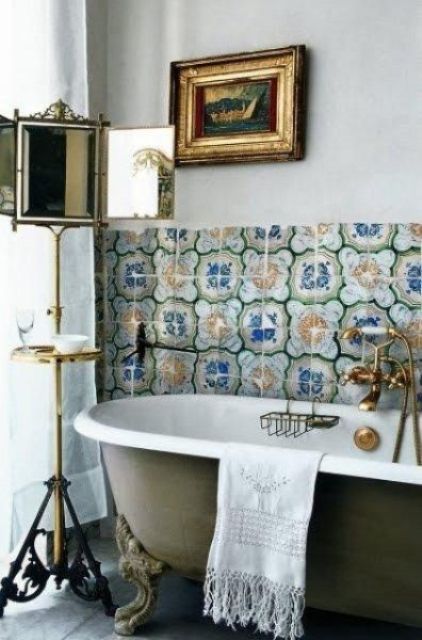a refined vintage bathroom with bold and colorful Moroccan tiles, a vintage olive green clawfoot tub, a vintage mirror on a stand and a vintage artwork