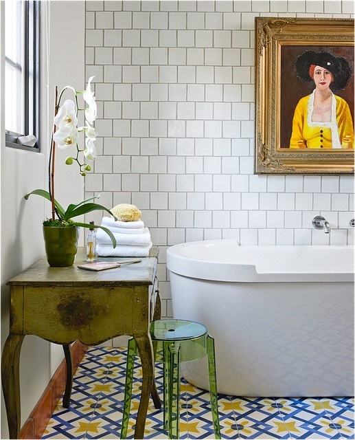 a beautiful eclectic bathroom with square white tiles, a bold Moroccan tile floor, a vintage green vanity, a modern tub and a vintage artwork