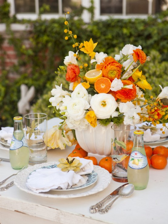 a bright and chic wedding tablescape with orange, yellow and white blooms, neutral textiles and some fruit right on the table
