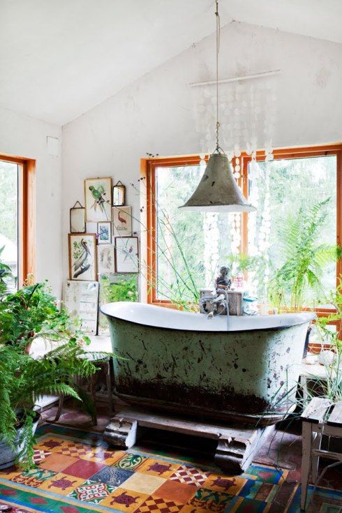 a boho bathroom with large windows, a shabby chic tub ona  raised platform, a bright multi-color tiled floor, potted plants and a gallery wall