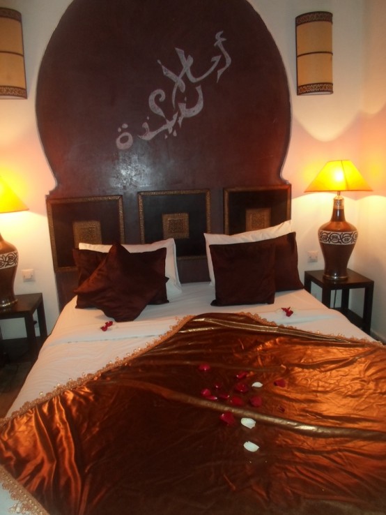 a Moroccan bedroom done in rust, brown and neutrals, with ornate lamps and a statement artwork on the wall