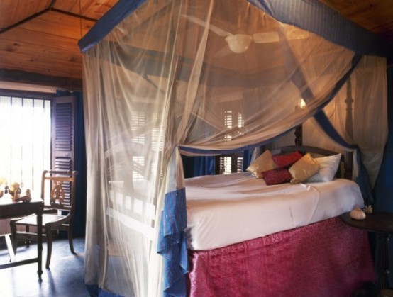 a bedroom with dark stained wood, a carved wooden bed and sheer and colored cnaopy in layers over the bed