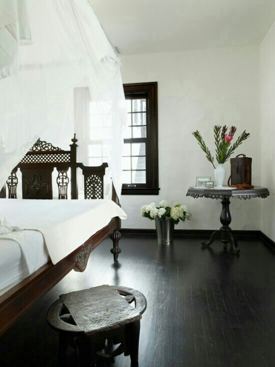 a monochromatic bedroom with a carved wodoen bed, chair and table and neutral bedding and a canopy