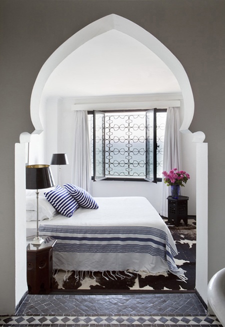 a contrasting Moroccan bedroom in an alcove, an ornate window, a carved wooden table and a faux animal skin