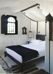 a black and white Moroccan bedroom with a shuttered window, a dark stained bed, a canopy and hanging lanterns