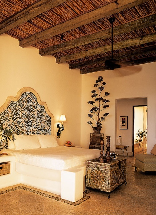 a neutral Moroccan bedroom with an ornate bed, a carved wooden chest with decor and a potted plant