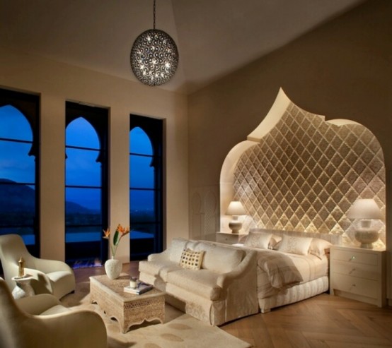 a luxurious Moroccan bedroom with a carved out headboard wall, Moroccan-inspired windows and a carved wooden table