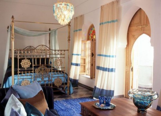 an elegant Moroccan bedroom done in blues and gold, with a gold bed, ornate wooden shutters and blue textiles here and there