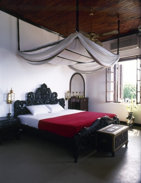 a Moroccan bedroom with a black carved bed and chest, gold lanterns and a canopy floating in the air