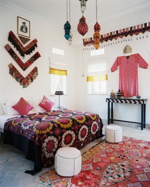 a colorful Moroccan bedroom with bright lanterns, printed rugs and bedding, a colorful artwork of fabric