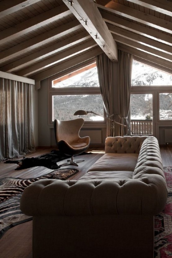 a contemporary chalet living room with a glazed wall for the view, a large neutral sofa and a leather chair, neutral curtains and animal skin rugs