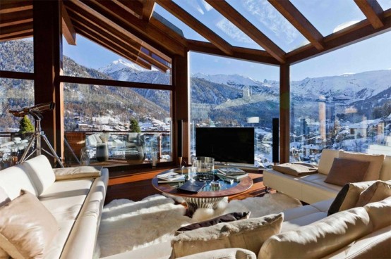 a luxurious contemporary chalet living room with glazed walls and a roof to enjoy the views, neutral seating furniture and a round glass coffee table is wow