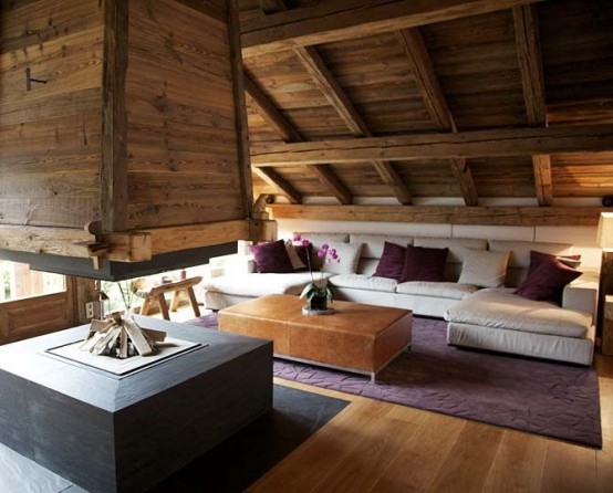 a contemporary chalet living room clad with wood, with an open hearth, a white sofa, a leather ottoman and some purple pillows