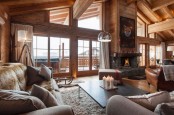 a modern chalet living room with wooden beams, a fireplace, some neutral seating furniture and leather chairs, pendant lamps and candles