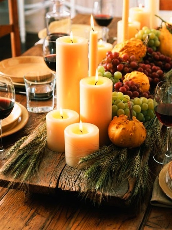 a natural Thanksgiving tablescape with an uncovered table, neutral porcelain, a wooden bowl with candles, greenery and frapes