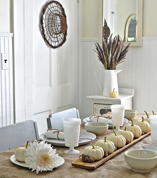 a wooden board with white pumpkins and acorns, feathers and wheat for a chic and all-natural Thanksgiving table