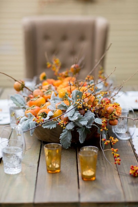 a natural Thanksgiving tablescape with an uncovered table, a pretty persimmon centerpiece with pale greenery and twigs and colored glasses is very elegant and chic