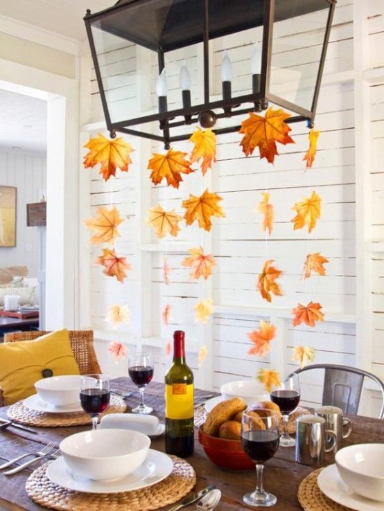 a natural Thanksgiving tablescape with woven chargers, fall leaves hanging down from the chandelier, metallic mugs and classic white porcelain