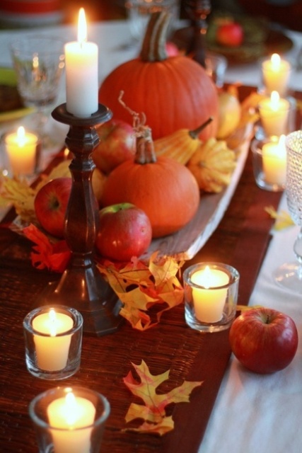 a natural Thanksgiving tablescape with fall leaves, bright pumpkins and apples and lots of candles is a lovely and bold idea for your family dinner