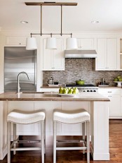 a modern white kitchen with shaker cabinets, stone countertops and a tile backsplash, pendant lamps and upholstered stools