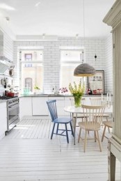 a white Scandinavian kitchen with only lower cabinets, white subway tiles, a table and mismatching chairs, a pendant lamp and lots of light