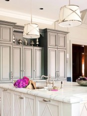 an elegant kitchen with grey cabinets and a white kitchen island, pendant lamps and white countertops plus elegant fixtures