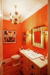 an orange powder room with a chandelier, bright artworks, orange lamps and a floral vanity