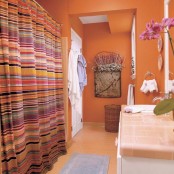 a rust-colored bathroom with a warm-colored floor and a bright striped curtain that includes orange touches