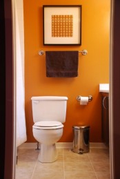 a small bathroom with orange walls and a matching artwork to create a bright and vivacious look