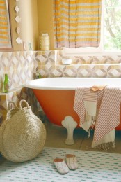a bright orange bathtub and a matching striped curtain and various prints incorporated create a bold and bright bathing space