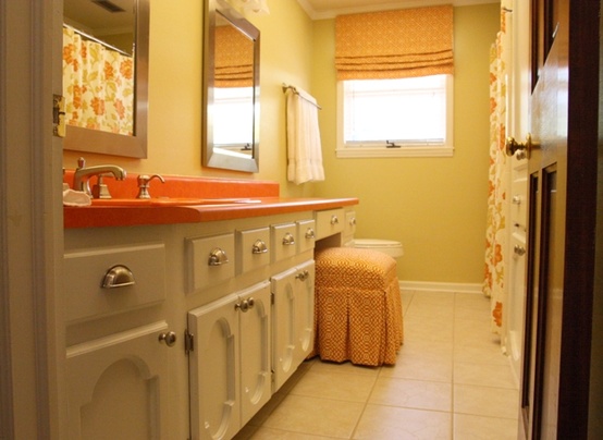 an orange countertop adds color to the neutral vanity and an orange printed shade and stool make the space more interesting