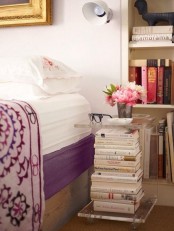 a bedside table made of a stack of books in an acrylic cover, wiht a bright floral arrangement is a great idea for a book-lover