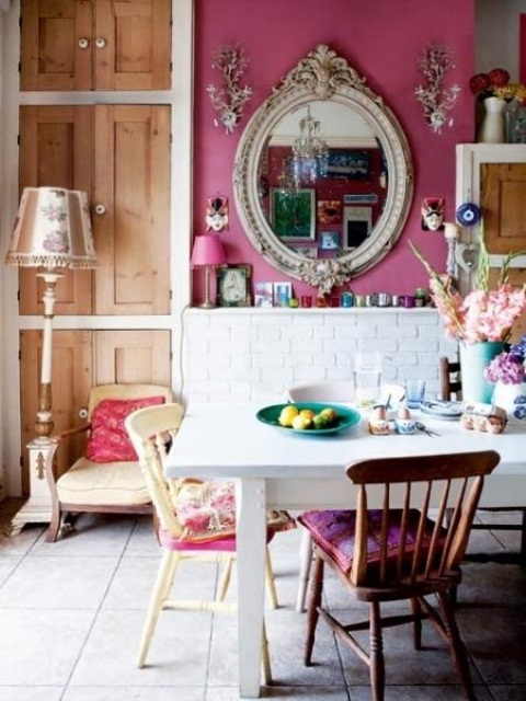 a colorful eclectic dining space with pink and white brick walls, colorful mismatching chairs, a mirror in a vintage frame and a floor lamp