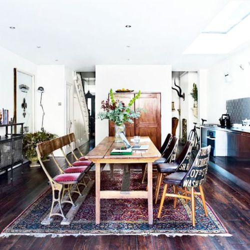 a bright boho dining room with a boho rug, pink and purple chairs, vintage rustic wooden furniture