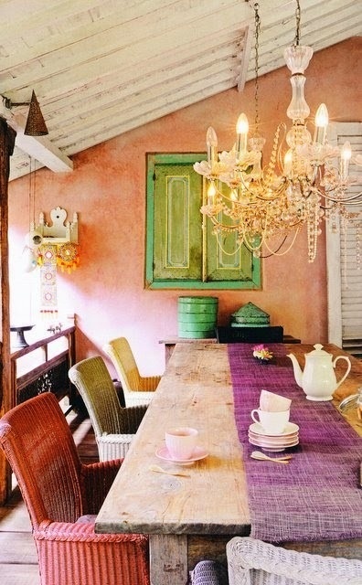 a bright boho dining room with a vintage chandelier, a rustic wooden table, colorful wicker chairs and touches of mint