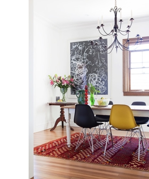 an eclectic boho dining room with a bold rug, vintage rustic furniture, a refined chandelier and colorful chairs