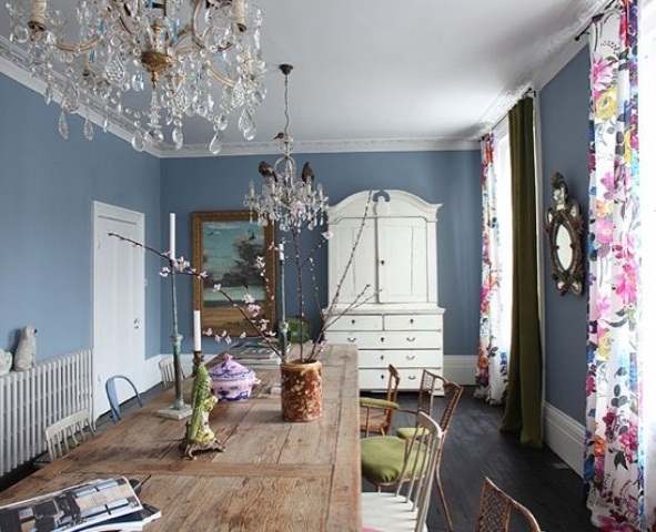 a romantic dining space with grey walls, floral curtains, a rustic dining table and mismatching chairs