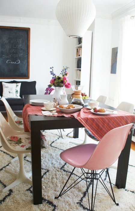 a modern dining room with a black dining table, a white wicker lamp and mismatching chairs
