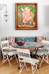 a colorful eclectic space with a bright artwork, mismatching printed pillows, white forged chairs and a checked table