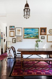 a boho dining room with a bold red rug, a Moroccan lamp, dark staiend furniture and a gallery wall