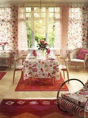 a cozy and bright dining room with lots of pink and red and floral patterns plus a wicker lamp