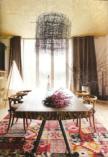 a unique dining room with a wooden table, stylish chairs, a bright boho rug and a whimsical chandelier