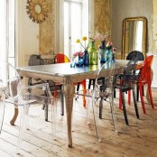 a bright eclectic dining room with colorful mismatching chairs, neutral and wallpaper walls, large mirrors and a vintage table