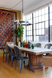 an eclectic dining room with a wooden table, metal and leather chairs, a boho rug on the wall