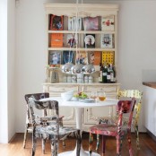 a vintage meets shabby chic dining room with mismatching bright chairs, a chic bookcase and a simple round table