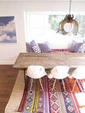 a boho meets rustic dining space with a wooden table, white modern chairs, a colorful boho rug and pillows