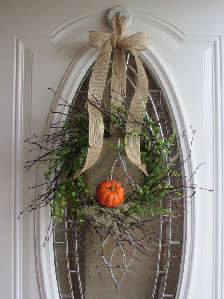 a cool twig fall wreath with greenery, moss, a faux pumpkins and a burlap bow on top is a cool fall decoration