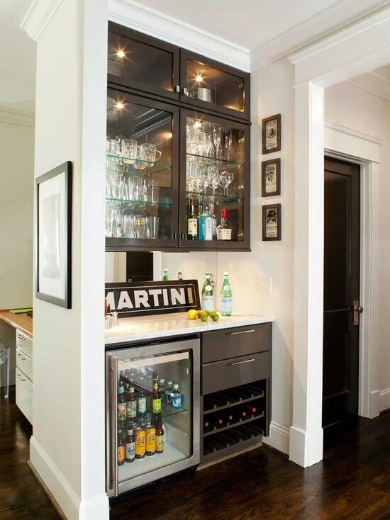 an awkward nook turned into a built-in bar, with glass storage cabinets, a mini fridge and drawers and storage units, a mirror and lemons and bottles is a cool idea to rock