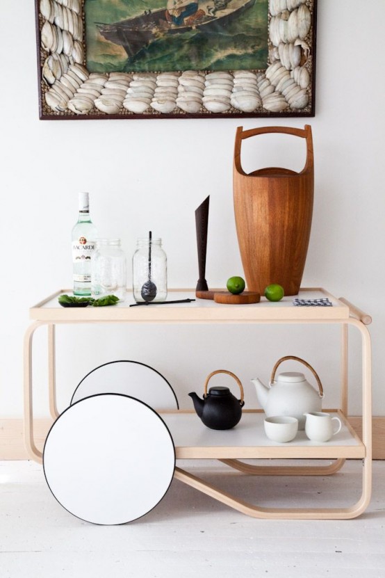 a contemporary home bar cart of stained wood, with oversized white wheels, candles, bottles, decanters and tea pots