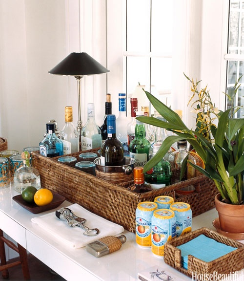 a relaxed tropical home bar with potted plants, elegant table lamps, a woven tray with wine bottles and glasses